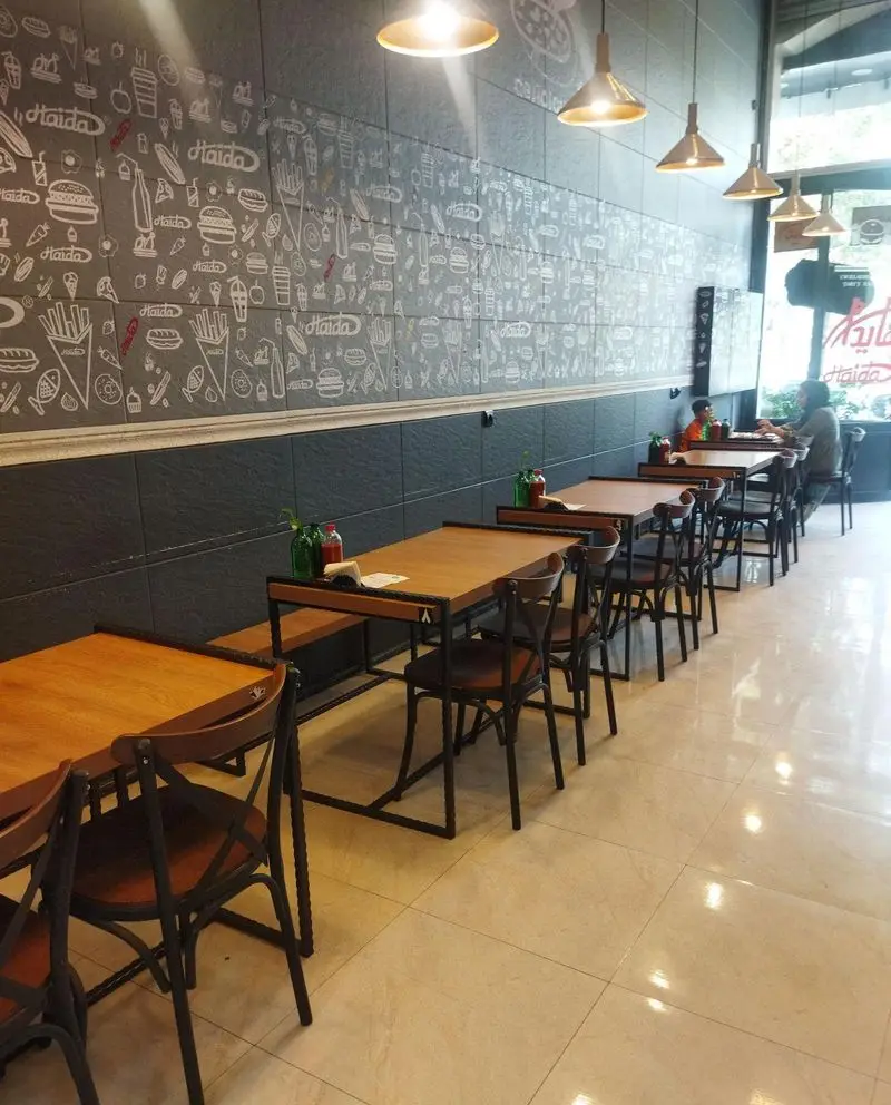 دکوراسیون شیک و فضای داخلی دلنشین فست فود هایدا پیروزی با دیوارهای طرح‌دار فست‌فودی، میز و صندلی‌های چوبی برای تجربه غذای لذت‌بخش.