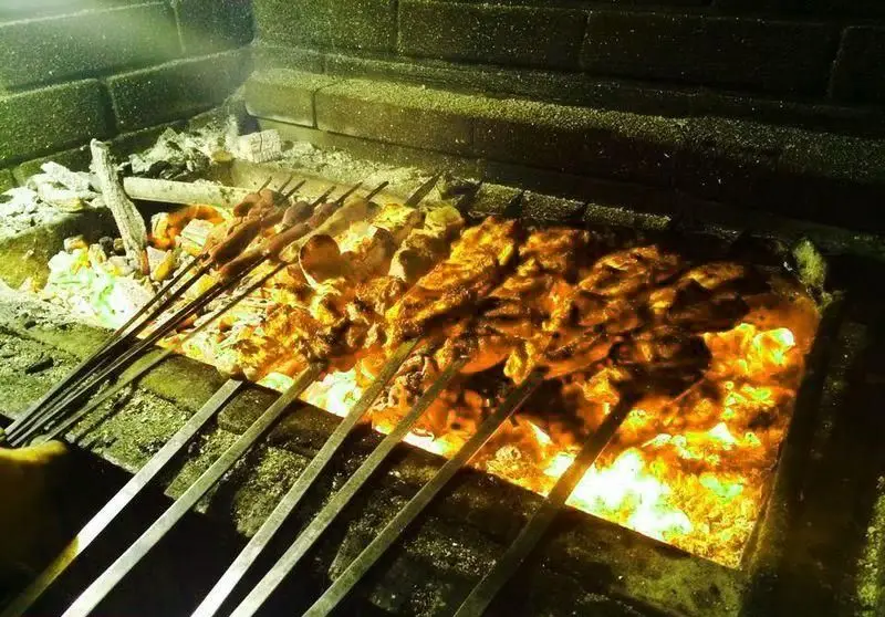 سیخ‌های کباب‌های خوشمزه و تازه در حال کباب شدن روی زغال داغ در منقل کباب شب زدگان. آماده سرو برای یک وعده غذایی لذیذ.