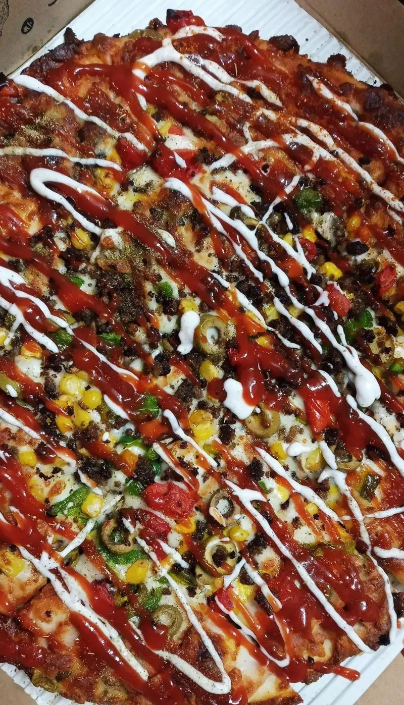 پیتزا پرملات و خوشمزه فست فود مزه با سس کچاپ، سس سفید، گوشت چرخ کرده، ذرت، فلفل دلمه‌ای و زیتون، آماده سرو در جعبه.