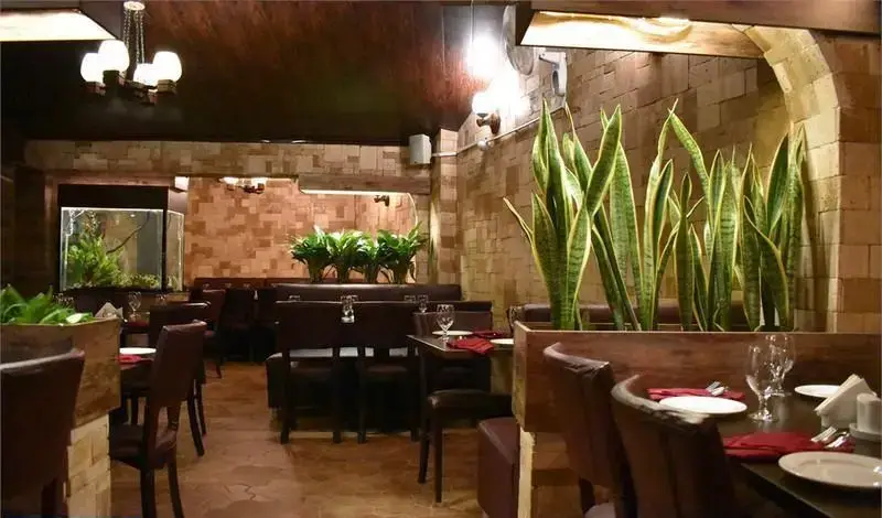 فضای داخلی جذاب رستوران ایتالیایی ترامونتو با دکوراسیون دیوارهای آجری، سقف چوبی، میز و صندلی‌های شیک، آکواریوم بزرگ و گلدان‌های گیاه.