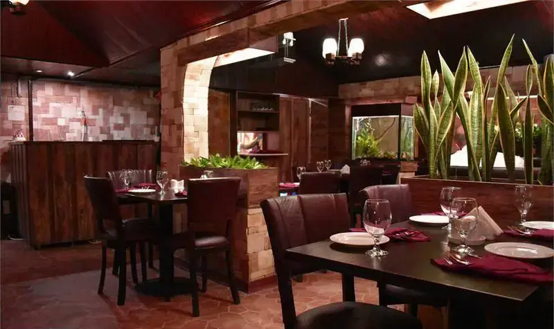 نمایی از فضای داخلی گرم و دلپذیر رستوران ایتالیایی ترامونتو با میزهای غذاخوری چوبی آماده پذیرایی، دکوراسیون سنگی، آکواریوم و گیاهان طبیعی.