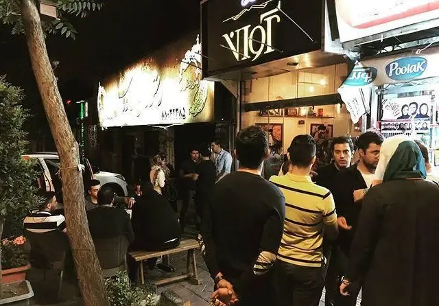 تصویری شبانگاهی از فست فود آوانت که مشتریان زیادی را در فضای بیرونی و دنج خود گرد هم آورده است، محیطی پرجنب و جوش و دلنشین.