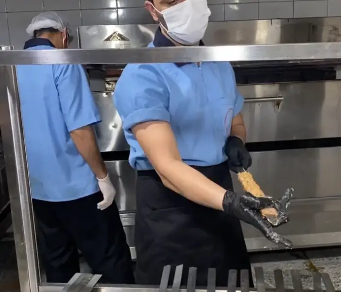 کترینگ ارغوان: آشپزها در حال آماده سازی کباب لذیذ در آشپزخانه صنعتی با تجهیزات مدرن، رعایت کامل بهداشت و پروتکل‌های ایمنی غذا.