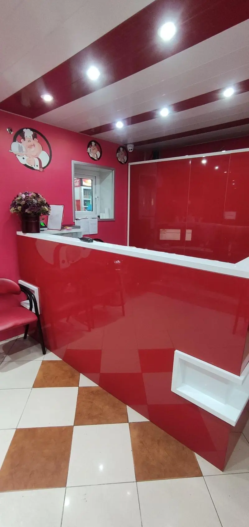 نمای داخلی شیک کترینگ ارغوان با پیشخوان قرمز مدرن، دکوراسیون جذاب با تصاویر سرآشپز و سقف نواری قرمز و سفید برای تجربه دلپذیر سفارش غذا.