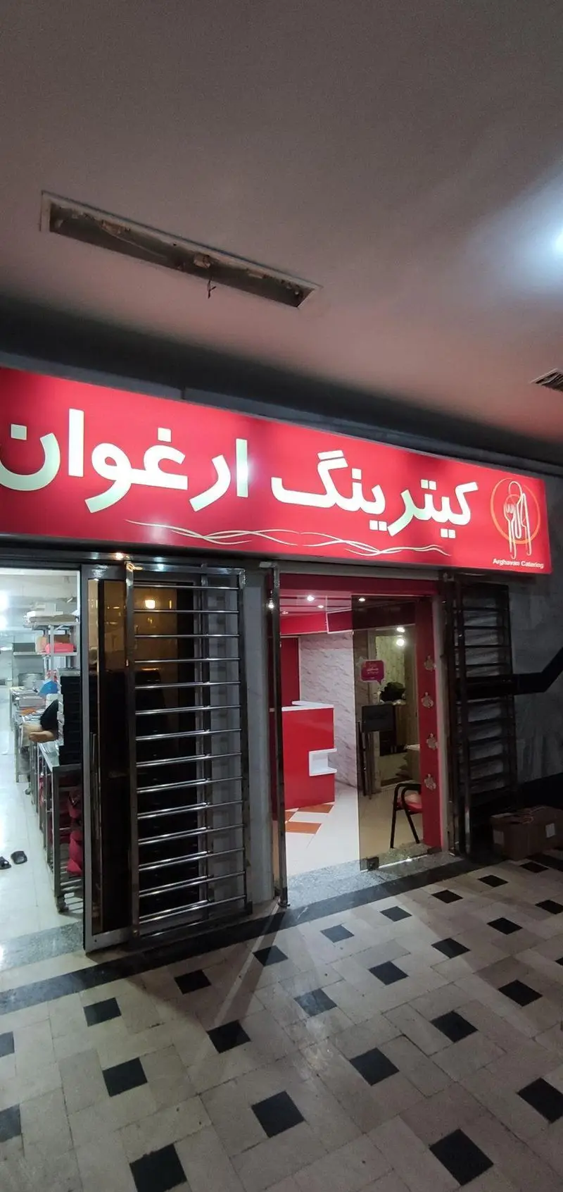 نمای بیرونی کترینگ ارغوان با تابلوی درخشان و لوگوی قاشق و چنگال، نشان‌دهنده خدمات پذیرایی و تهیه غذای باکیفیت و تازه.