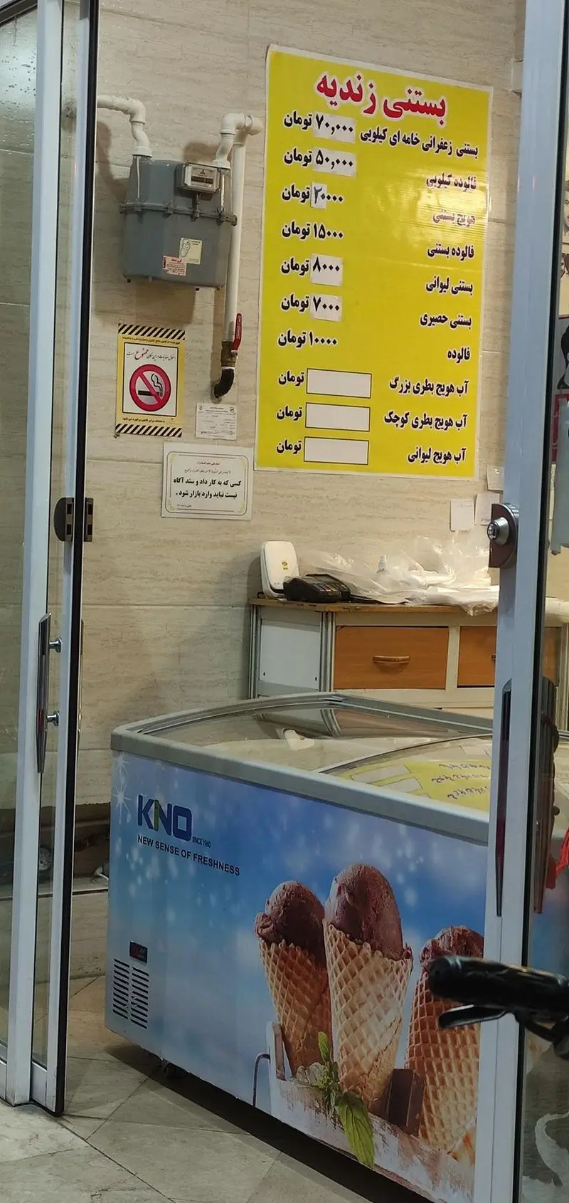 منوی بستنی فروشی زندیه شامل قیمت بستنی زعفرانی، فالوده، آب هویج و فریزر بستنی قیفی KNO در فضای داخلی مغازه.