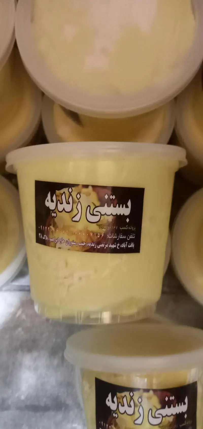 تصویری از چندین ظرف آماده بستنی سنتی زرد رنگ از بستنی فروشی زندیه، با برچسب مشخصات، تلفن و آدرس سفارش.