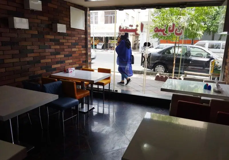 فضای داخلی مدرن و دنج پیتزا میزبان با دیوار آجری، میز و صندلی‌های شیک، ایده‌آل برای دورهمی‌ها و صرف پیتزا در محیطی صمیمی.