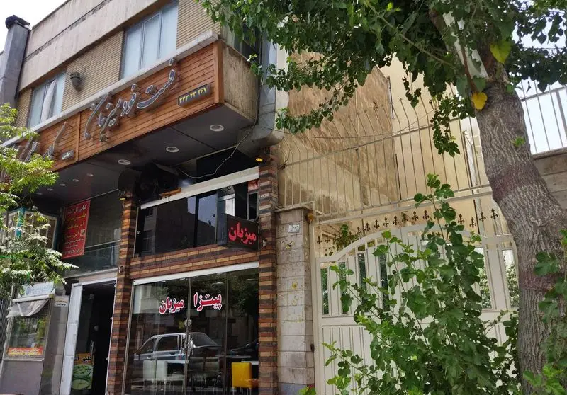 نمای بیرونی و تابلوی فست فود و پیتزا میزبان، محلی دنج برای تجربه طعم لذیذ انواع پیتزا و غذاهای آماده.