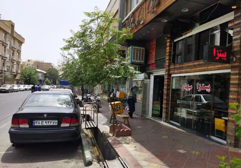 پیتزا میزبان، یک فست فود محبوب در خیابان شلوغ شهر، با ویترین شیشه‌ای بزرگ، تابلوی روشن و مشتریان در حال تردد، همراه با خودروهای پارک شده.