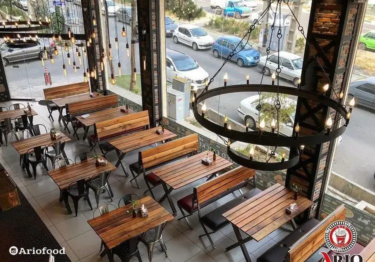 فضای رستوران مرغ سوخاری آریو: دکوراسیون داخلی مدرن با میز و نیمکت‌های چوبی، نورپردازی خاص و نمای دلنشین خیابان.