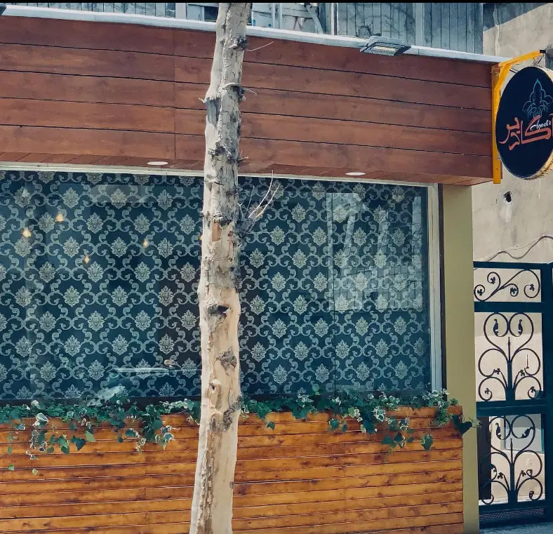 نمای بیرونی کافه حوروش با دکوراسیون چوبی شیک، پنجره‌ای با پرده طرح‌دار، و گلدان‌های سبز. تابلوی نام کافه به وضوح دیده می‌شود.