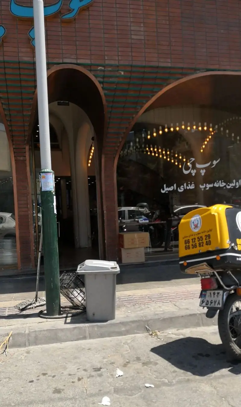 نمای بیرونی رستوران سوپ چی با تابلوی اولین خانه سوپ غذای اصیل و موتور تحویل غذا در کنار سطل زباله و تیر چراغ برق
