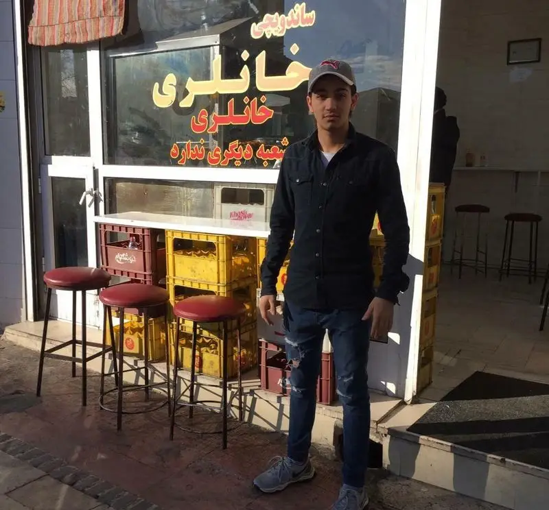 تصویری از یک پسر جوان در مقابل ورودی ساندویچی خانلری، یک فست فود محبوب با تابلویی که اعلام می‌کند شعبه دیگری ندارد.