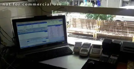 تصویری از میز کار و سیستم مدیریت سفارشات تهیه غذا خانه تست، با دستگاه‌های کارتخوان و منظره بیرون مغازه با نیمکت.