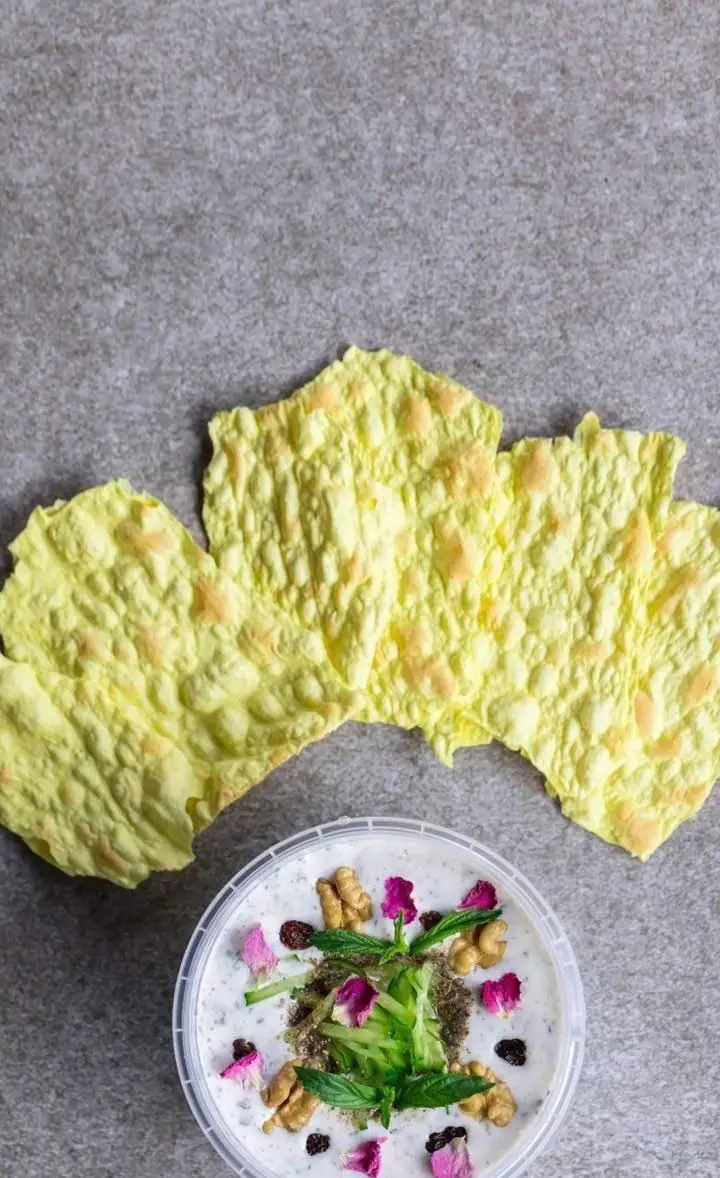 ماست و خیار سنتی فست فود دیبان با تزئینات گل محمدی، گردو و نعناع، همراه با نان خشک ترد و خوشمزه، گزینه‌ای عالی برای پیش غذا.