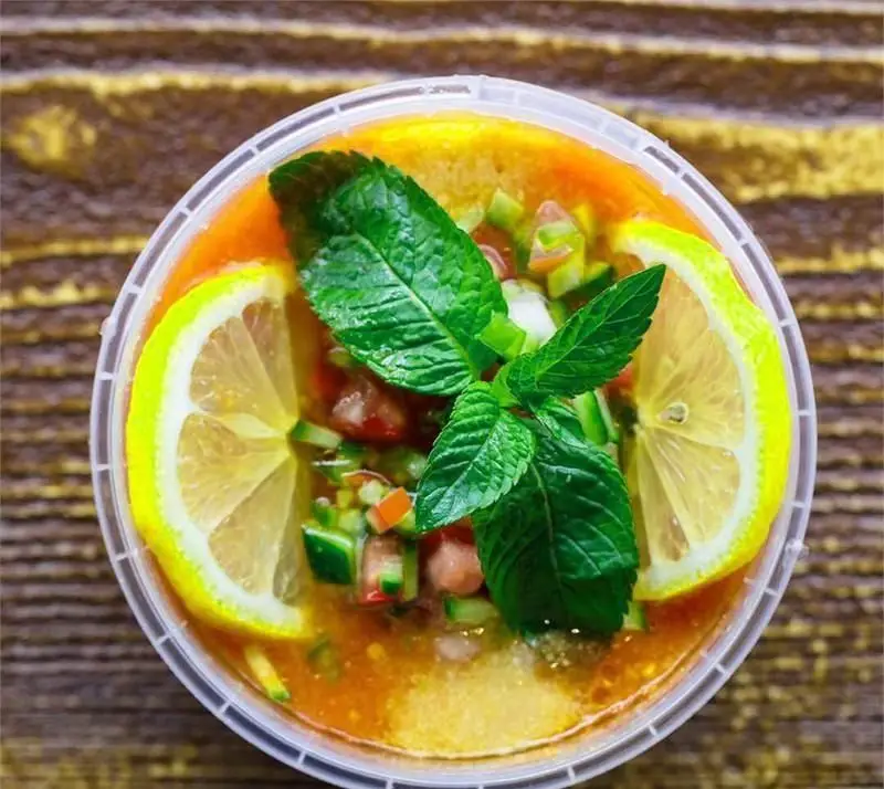 تصویری از یک سوپ یا سالاد تازه و سالم در ظرف شفاف از فست فود دیبان، تزئین شده با لیمو و نعناع تازه. غذایی اشتها آور و خوشمزه.