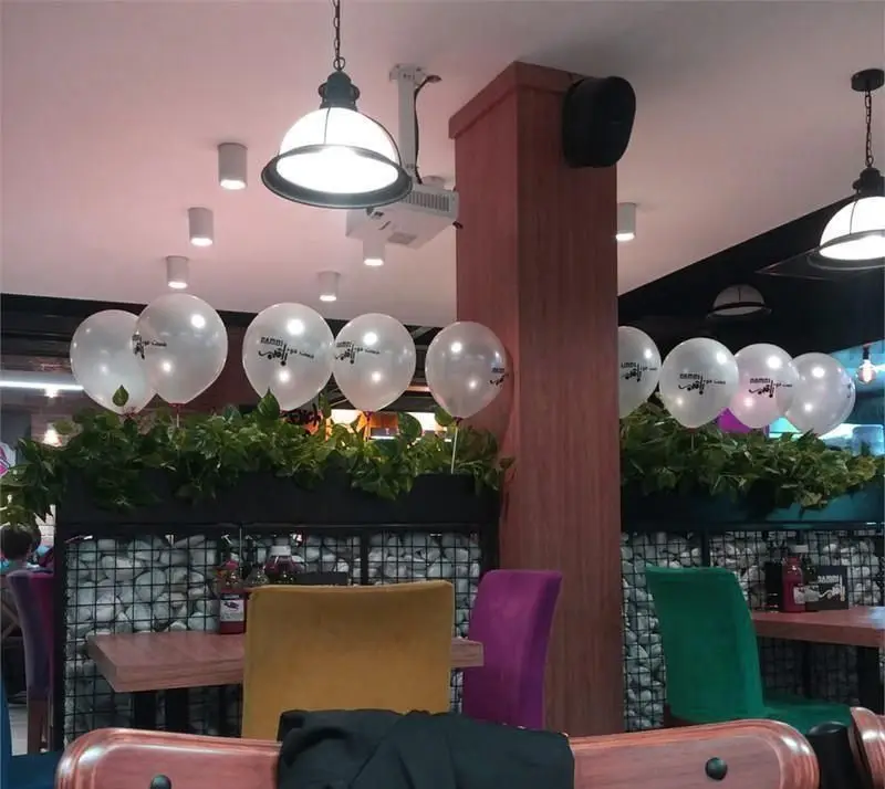 فضای داخلی فست فود بامبی فود با دکوراسیون شیک، شامل میز و صندلی‌های رنگی، گلدان‌های سبز و بادکنک‌های لوگودار بامبی فود.