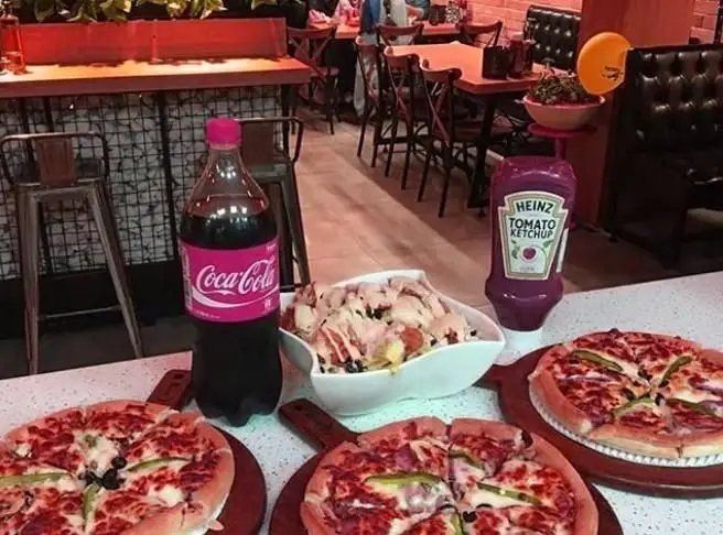 نمایی اشتهاآور از میز پیتزا، نوشابه کوکاکولا و کچاپ هاینز در فست فود بامبی فود، برای تجربه‌ای لذیذ در محیطی دلنشین.