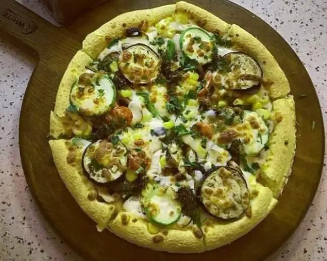 پیتزا سبزیجات تازه بامبی فود با کدو سبز، ذرت و سبزیجات معطر، روی تخته چوبی، مناسب برای یک وعده غذایی سالم و خوشمزه در فست فود بامبی فود.