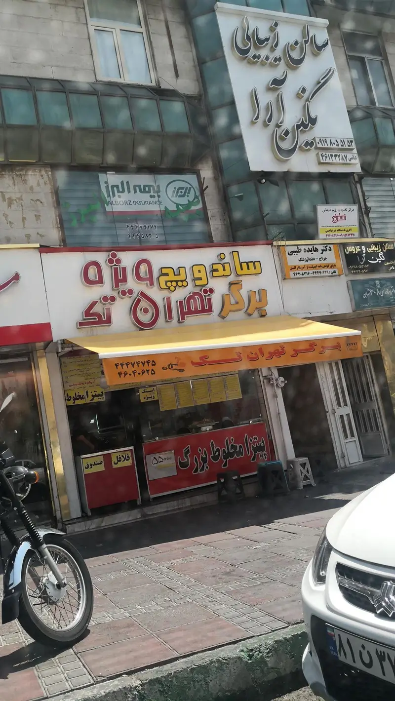 تصویر نمای بیرونی فست فود برگر تهران تک در کنار سالن زیبایی گلشن آرا و بیمه البرز در خیابان شهر.