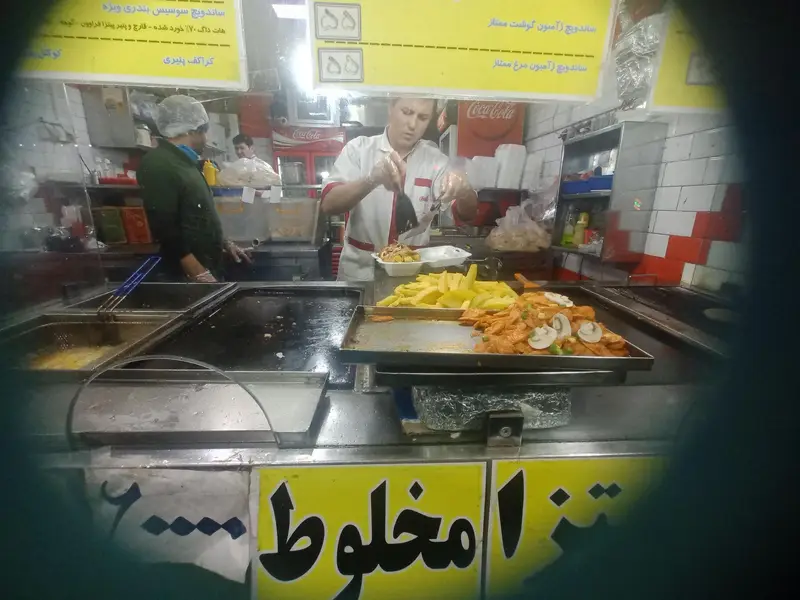 نمایی از آشپزخانه فست فود برگر تهران تک در حال آماده سازی انواع غذاها، از جمله سیب زمینی سرخ کرده و ساندویچ، توسط کارکنان.