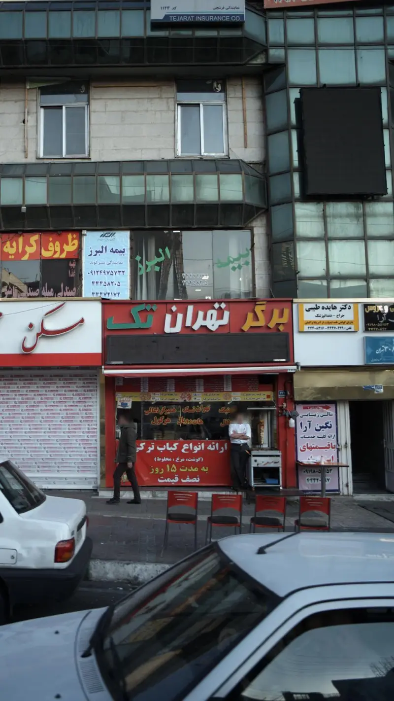 فست فود برگر تهران تک با منوی کباب ترکی، در نمای شهری پرجنب‌وجوش با ساختمان‌ها و خودروهای پارک شده.