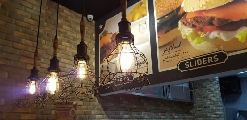 فضای داخلی مدرن و جذاب رستوران گامبی با دیوارهای آجری، چراغ‌های آویز طرح صنعتی و منوی اسلایدرهای ۱۰۰٪ گوشت خالص.