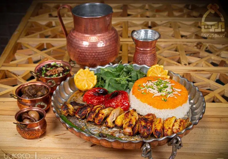 میز غذای سنتی رستوران برکت: جوجه کباب، پلو زعفرانی، گوجه کبابی، سبزیجات و مخلفات لذیذ ایرانی در ظروف مسی