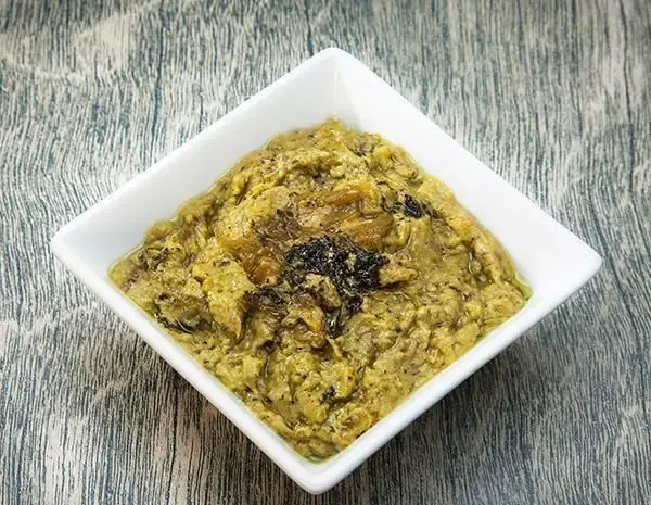 یک کاسه سفید پر از خوراک بادمجان رژیمی یا پیش غذای لذیذ ایرانی رستوران برکت، با تزئین پیاز داغ روی میز چوبی.