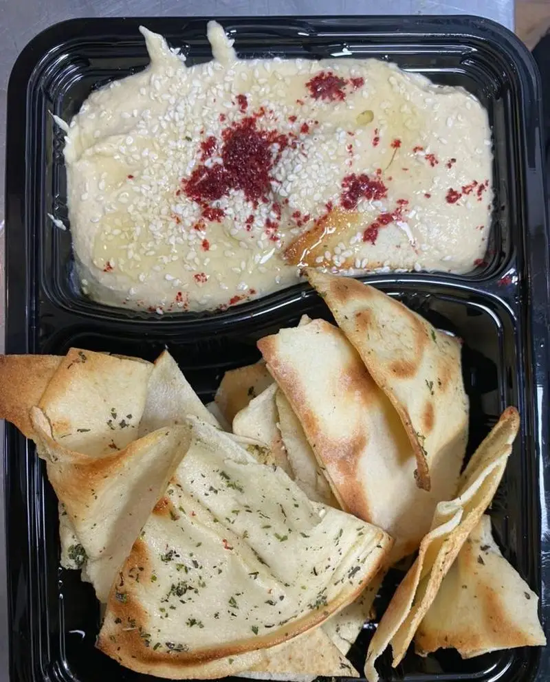 هوموس تزئین شده با کنجد و سماق، و نان پیتا برشته سبزیجات از رستوران برکت (ایرانی فرنگی رژیمی صبحانه). پیش غذای سالم.