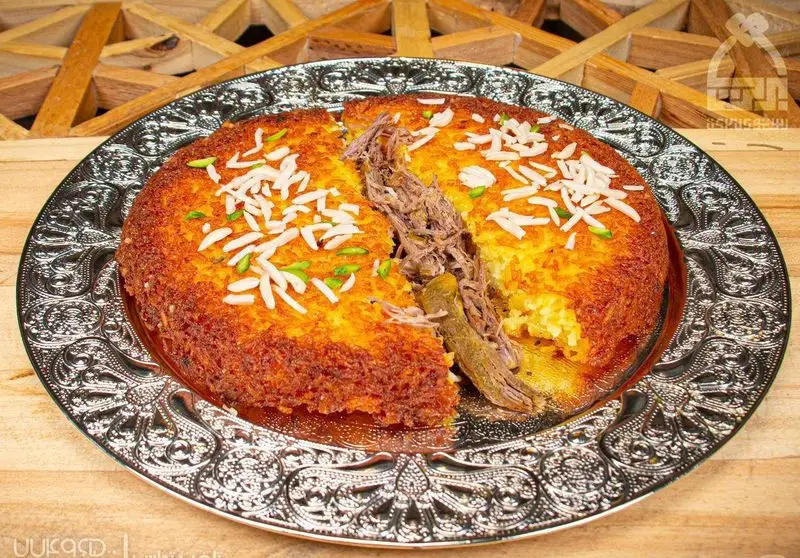 تصویری از ته‌چین گوشت و برنج زعفرانی خوشمزه و سنتی رستوران برکت؛ یک غذای اصیل ایرانی با ته دیگ طلایی عالی روی سینی نقره‌ای.