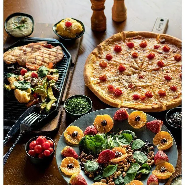 میز مجلل غذای کافه رستوران نارکو شامل پیتزا گوجه‌ای، مرغ گریل، سبزیجات تازه، سالاد میوه و مغز، و انواع دیپ‌های سالم و خوشمزه.