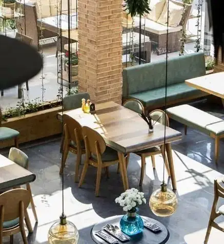 دکوراسیون داخلی دنج و شیک کافه رستوران نارکو با میز و صندلی‌های چوبی، مبلمان سبز و نورپردازی دلنشین برای مشتریان.