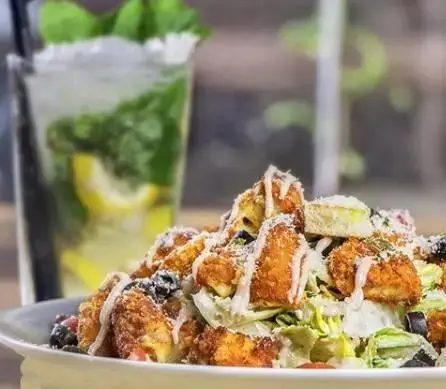 تصویری جذاب از سالاد سزار با تکه‌های مرغ سوخاری ترد و خوشمزه به همراه نوشیدنی موهیتو خنک در محیط دلنشین کافه رستوران نارکو.