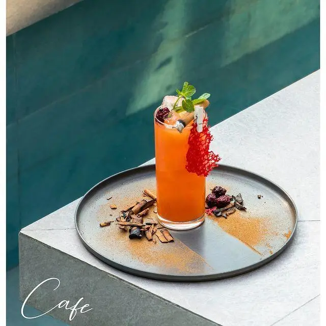 کوکتل میوه‌ای پرتقالی کافه رستوران نارکو، با گارنیش نعنا و توت، روی سینی کنار استخر سرو شده برای لحظات تابستانی.