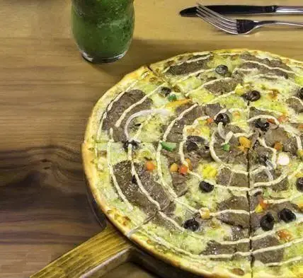 پیتزا گوشت و زیتون خوشمزه کافه رستوران نارکو بر روی میز چوبی همراه با نوشیدنی سبز. لذت یک وعده غذایی عالی در نارکو.