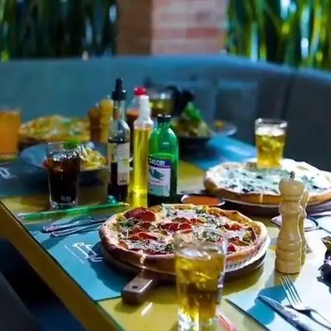 میز جذاب و پر از خوراکی‌ها در کافه رستوران نارکو با پیتزاهای متنوع، نوشیدنی‌های خنک و چاشنی‌های سس برای تجربه یک غذای عالی.