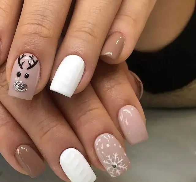 طراحی ناخن زمستانی و کریسمس شیک با طرح گوزن شمالی نگین‌دار، دانه برف سفید و لاک‌های قهوه‌ای، سفید و کرم نود دخترانه