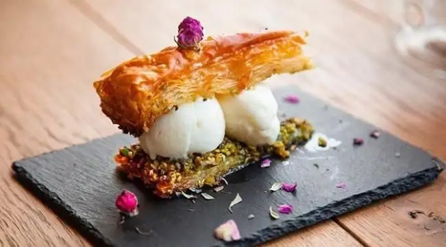 دسر باقلوای پسته ای کافی شاپ محفل با بستنی، گل محمدی و سینی سنگی. تجربه طعمی به یادماندنی.