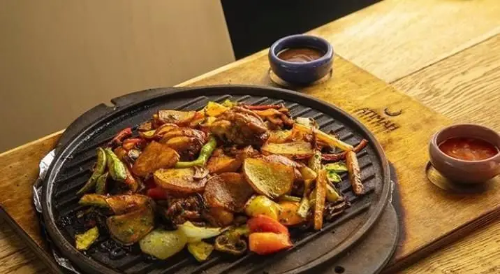 بشقاب ساج داغ کافی شاپ محفل با مرغ و سیب زمینی کبابی، فلفل و سبزیجات تازه. یک غذای گرم و لذیذ برای تجربه ای دلنشین.