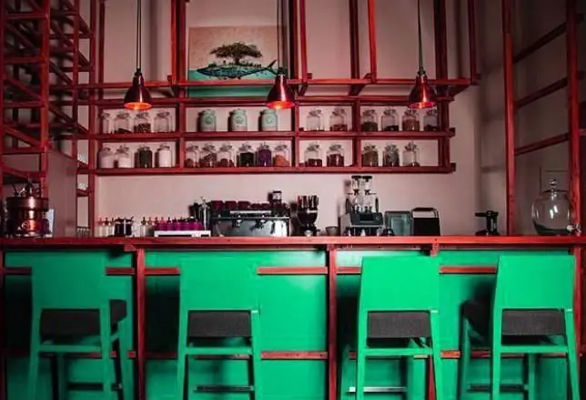 نمایی از کانتر اصلی کافی شاپ محفل با طراحی رنگارنگ سبز و قرمز، بار استول‌های مدرن، دستگاه‌های قهوه و قفسه‌های زیبای ادویه و قهوه.