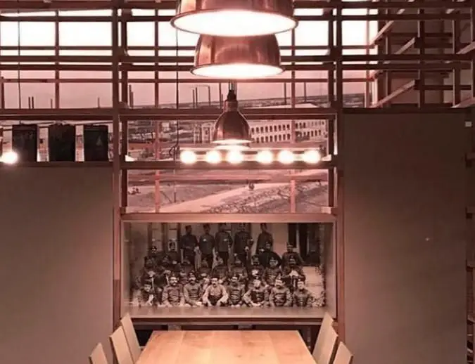 فضای داخلی کافی شاپ محفل با لوسترهای مسی، میز چوبی، و عکس‌های تاریخی جذاب، مکانی ایده‌آل برای دورهمی و تجربه دلنشین.