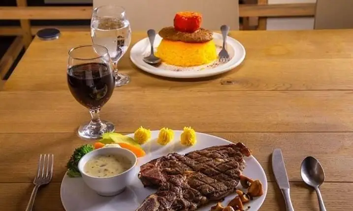 تجربه یک شام دلپذیر در کافی شاپ محفل: استیک گریل شده با سس، سبزیجات و پلو زعفرانی همراه با نوشیدنی‌های متنوع در محیطی آرام.