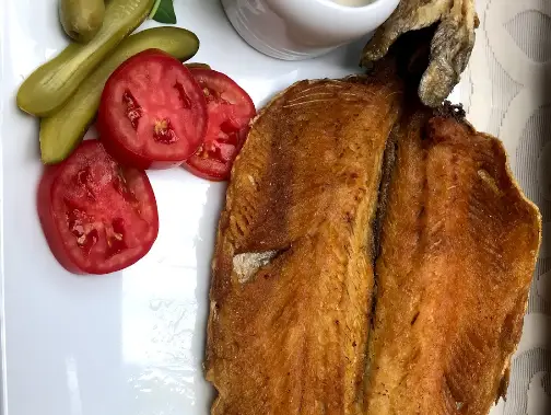 ماهی سرخ شده لذیذ و طلایی، سرو شده در رستوران هتل بلوط، همراه با گوجه فرنگی تازه، خیارشور ترد و سس مخصوص.