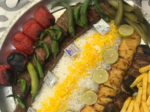 سینی چلو کباب و جوجه کباب خوشمزه رستوران هتل بلوط شامل گوجه، فلفل، لیمو و سیب زمینی سرخ کرده، غذای اصیل ایرانی.