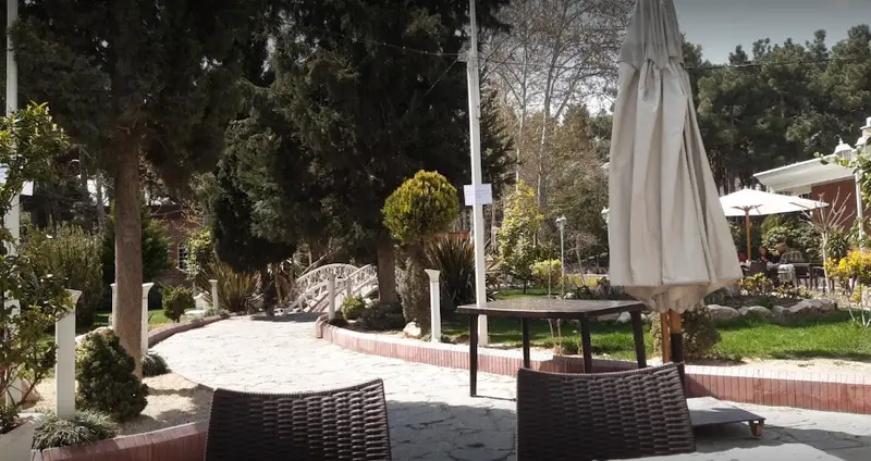 فضای باز و دلنشین رستوران هتل بلوط با میز و صندلی، چترهای آفتاب‌گیر، مسیر سنگی و باغ سرسبز مناسب صرف غذا در طبیعت