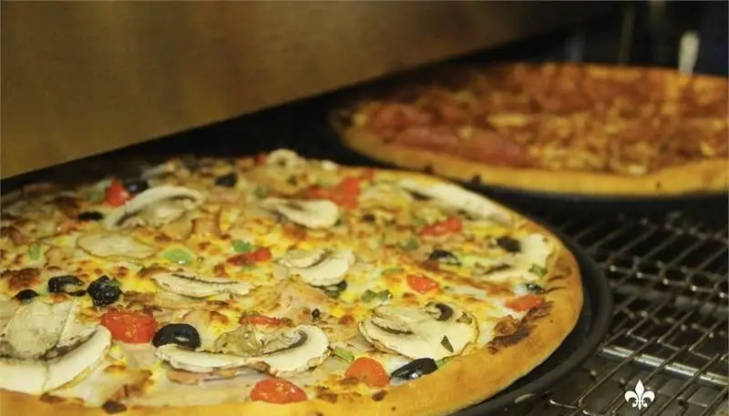 پیتزاهای داغ سیب360: پیتزای سبزیجات و قارچ با زیتون و فلفل در پیش‌زمینه، دیگری در حال پخت در فر، بسیار تازه و دلپذیر.