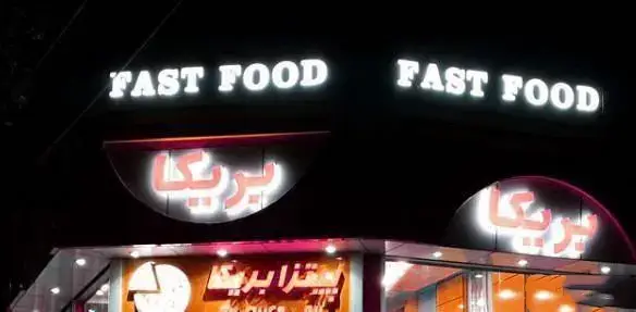 تصویر نمای بیرونی فست فود و پیتزا بریکا در شب با تابلوهای روشن "FAST FOOD" و نام "بریکا" به فارسی، یک مکان پرنور و جذاب.