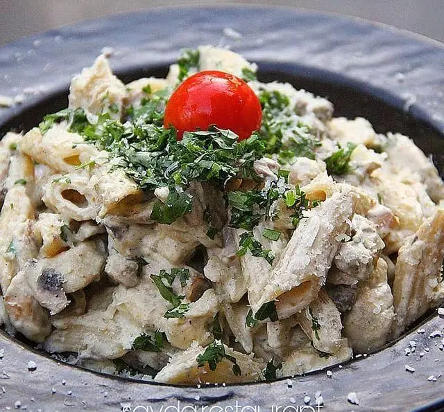 تصویر پاستا پنه خامه ای و قارچ تازه، با سس آلفردو، جعفری خرد شده و گوجه گیلاسی در ظرف مشکی. غذای ایتالیایی باغ رستوران سایدا شهران.